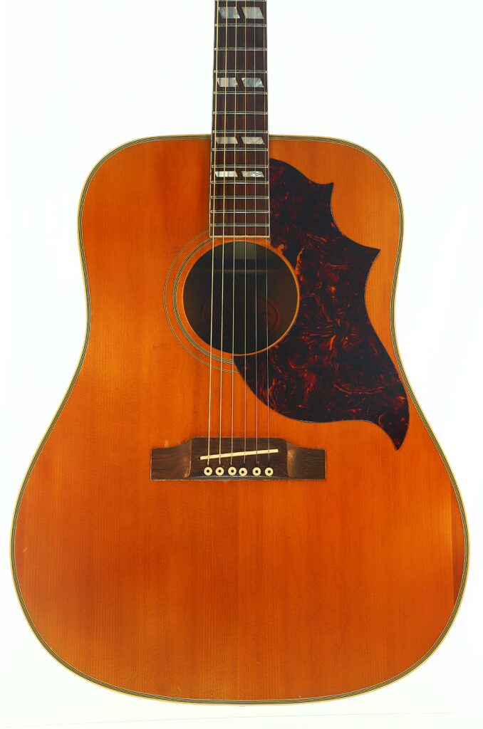 Eine Gibson SJN 1968 Akustikgitarre mit naturbelassener Holzoberfläche, einem dunklen Schildpatt-Schlagbrett und rechteckigen Einlagen auf dem Griffbrett, fotografiert vor weißem Hintergrund. Eine Gibson SJN 1968 Akustikgitarre mit naturbelassener Holzoberfläche, einem dunklen Schildpatt-Schlagbrett und rechteckigen Einlagen auf dem Griffbrett, fotografiert vor weißem Hintergrund.