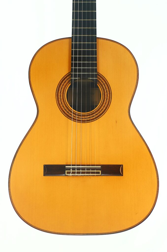 Die „Stefan Nitschke 2015 Friederich Klassische Gitarre“ mit einem Korpus aus Holz, sechs Saiten, einer aufwendig gearbeiteten Rosette um das Schallloch und einem dunklen Griffbrett ist vor einem schlichten weißen Hintergrund fotografiert. Die „Stefan Nitschke 2015 Friederich Klassische Gitarre“ mit einem Korpus aus Holz, sechs Saiten, einer aufwendig gearbeiteten Rosette um das Schallloch und einem dunklen Griffbrett ist vor einem schlichten weißen Hintergrund fotografiert.