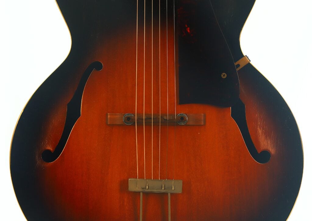 Nahaufnahme der Vorderseite einer Gibson L-48 Akustikgitarre aus dem Jahr 1948 mit Sunburst-Lackierung, Steg, Saiten und zwei f-förmigen Schalllöchern auf beiden Seiten des Instruments. Nahaufnahme der Vorderseite einer Gibson L-48 Akustikgitarre aus dem Jahr 1948 mit Sunburst-Lackierung, Steg, Saiten und zwei f-förmigen Schalllöchern auf beiden Seiten des Instruments.