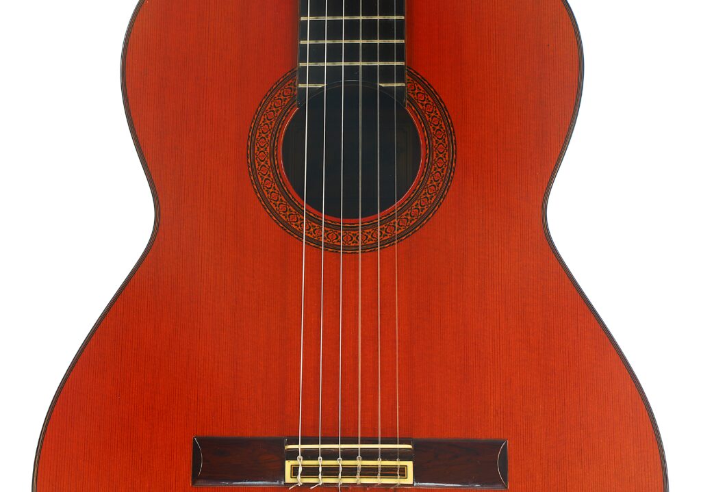 Nahaufnahme der Vorderseite einer klassischen Gitarre vom Typ „Jose Ramirez 1a 1977“ mit sechs Saiten, einem mit einer dekorativen Rosette verzierten Schallloch und einem rotbraunen Holzkorpus. Nahaufnahme der Vorderseite einer klassischen Gitarre vom Typ „Jose Ramirez 1a 1977“ mit sechs Saiten, einem mit einer dekorativen Rosette verzierten Schallloch und einem rotbraunen Holzkorpus.