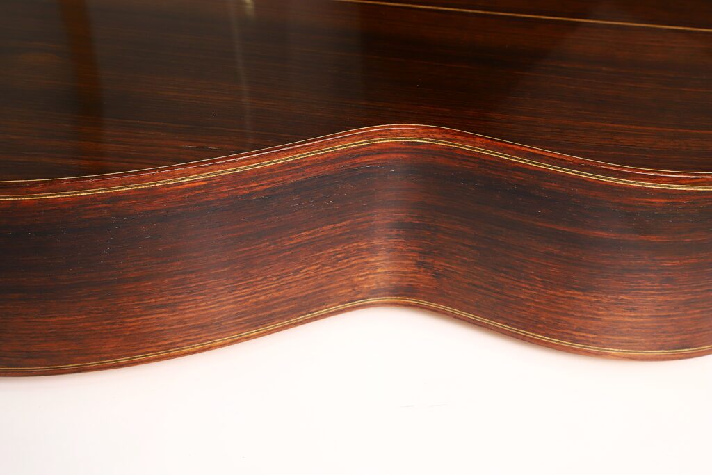 Nahaufnahme der Holzseite einer „Francisco Klassische Gitarre“ von Manuel Adalid Sr. aus dem Jahr 1971, die die satter Holzmaserung, die elegant geschwungene Form und die glatte Oberfläche hervorhebt. Nahaufnahme der Holzseite einer „Francisco Klassische Gitarre“ von Manuel Adalid Sr. aus dem Jahr 1971, die die satter Holzmaserung, die elegant geschwungene Form und die glatte Oberfläche hervorhebt.