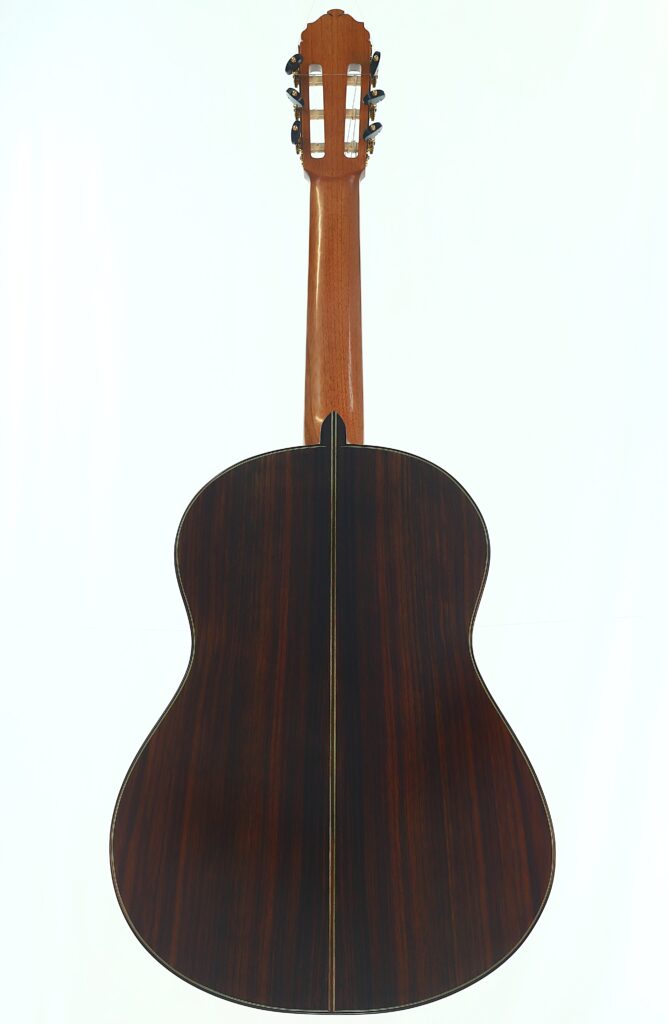 Rückansicht der „Gerhard Arns 2026 Smallman Klassische Gitarre“ mit einem Holzkorpus in dunkler Lackierung und einer Mittellinie, einem hellen Hals und Stimmwirbeln am Kopf, alles vor weißem Hintergrund. Rückansicht der „Gerhard Arns 2026 Smallman Klassische Gitarre“ mit einem Holzkorpus in dunkler Lackierung und einer Mittellinie, einem hellen Hals und Stimmwirbeln am Kopf, alles vor weißem Hintergrund.