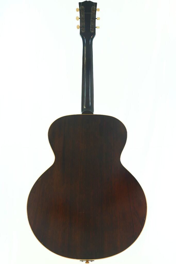 Das Bild zeigt die Rückansicht einer Gibson L-48 Akustikgitarre aus dem Jahr 1948 mit dunkler Holzoberfläche, abgerundetem Korpus und sechs Stimmwirbeln am Kopf, vor einem schlichten weißen Hintergrund. Das Bild zeigt die Rückansicht einer Gibson L-48 Akustikgitarre aus dem Jahr 1948 mit dunkler Holzoberfläche, abgerundetem Korpus und sechs Stimmwirbeln am Kopf, vor einem schlichten weißen Hintergrund.