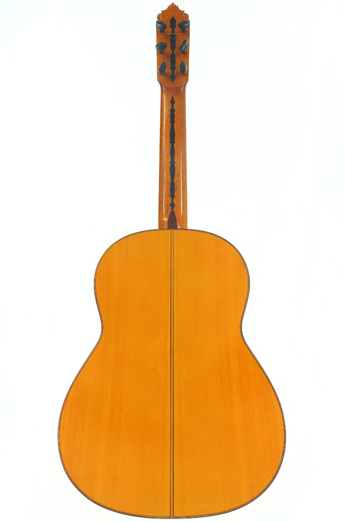 Die Rückansicht der Flamenco-Gitarre „Jeronimo Pena 1976“ besticht durch ihren Korpus aus hellem Holz, der durch eine schwarze Einlage in der Mitte und ein kunstvolles Muster aus dunklem Holz am Hals akzentuiert wird. Die Rückansicht der Flamenco-Gitarre „Jeronimo Pena 1976“ besticht durch ihren Korpus aus hellem Holz, der durch eine schwarze Einlage in der Mitte und ein kunstvolles Muster aus dunklem Holz am Hals akzentuiert wird.