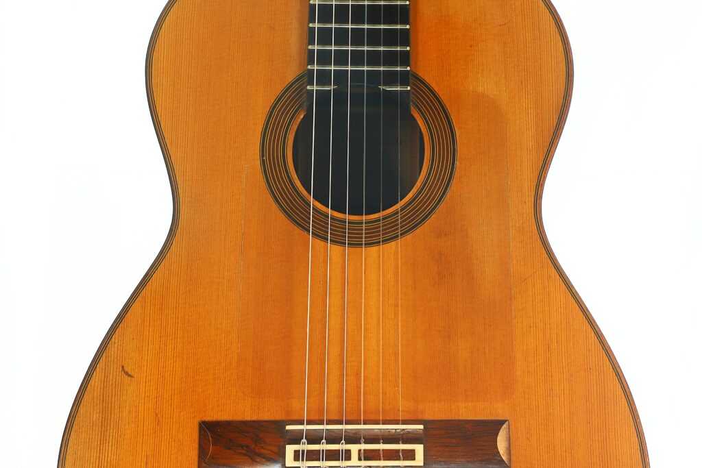 Nahaufnahme des Korpus und der Saiten einer Juan Lopez Aguilarte „Negra“ Flamenco-Gitarre aus dem Jahr 1984 mit Holzfinish, auf der das Schallloch und ein Teil des Stegs vor weißem Hintergrund zu sehen sind. Nahaufnahme des Korpus und der Saiten einer Juan Lopez Aguilarte „Negra“ Flamenco-Gitarre aus dem Jahr 1984 mit Holzfinish, auf der das Schallloch und ein Teil des Stegs vor weißem Hintergrund zu sehen sind.