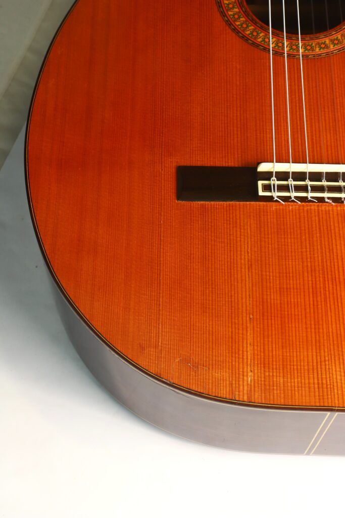 Detailansicht des Korpus und der Saiten der „Gran Klassische Gitarre“ von Raimundo y Aparicio Corujo vor hellem Hintergrund, wobei die Maserung des Holzes und ein Ausschnitt der Schalllochrosette besonders gut zur Geltung kommen. Detailansicht des Korpus und der Saiten der „Gran Klassische Gitarre“ von Raimundo y Aparicio Corujo vor hellem Hintergrund, wobei die Maserung des Holzes und ein Ausschnitt der Schalllochrosette besonders gut zur Geltung kommen.