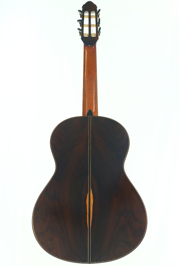 Die „Antonius Müller 2004 Doubletop Klassische Gitarre“ ist hier von hinten zu sehen: Sie besticht durch dunkles, poliertes Holz mit einer markanten Maserung und einer hellen Mittelnaht. Die „Antonius Müller 2004 Doubletop Klassische Gitarre“ ist hier von hinten zu sehen: Sie besticht durch dunkles, poliertes Holz mit einer markanten Maserung und einer hellen Mittelnaht.