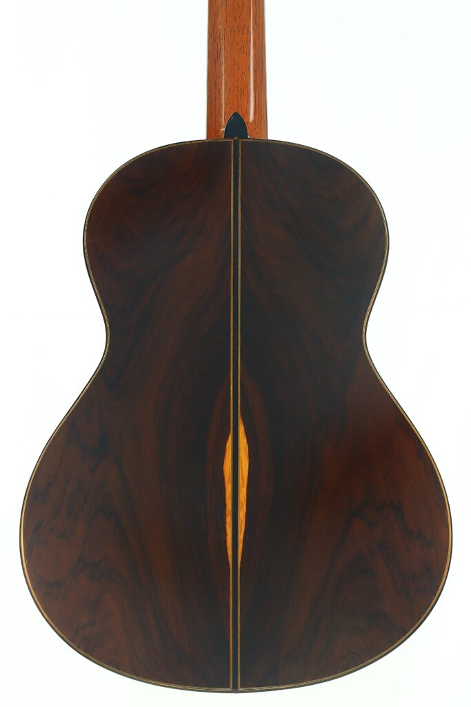 Rückansicht der „Antonius Müller 2004 Doubletop Klassische Gitarre“ mit satten, dunklen Holzmaserungen und einem helleren Mittelstreifen, der vertikal in der Mitte verläuft. Rückansicht der „Antonius Müller 2004 Doubletop Klassische Gitarre“ mit satten, dunklen Holzmaserungen und einem helleren Mittelstreifen, der vertikal in der Mitte verläuft.
