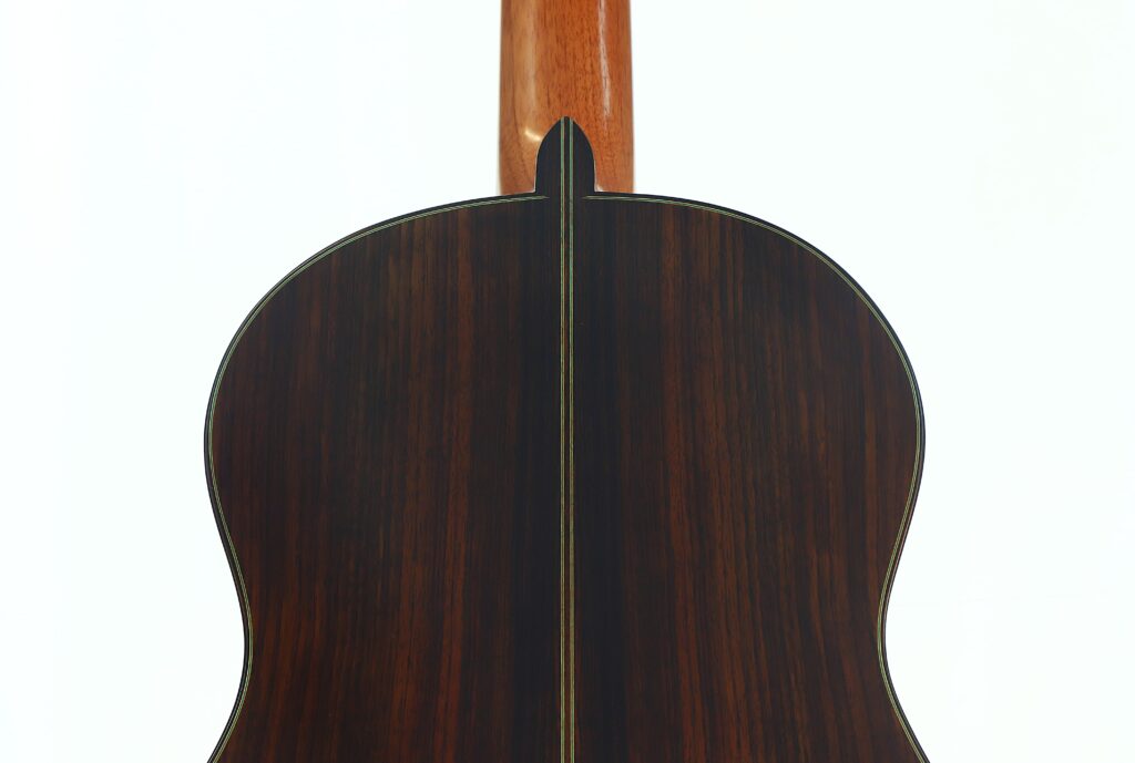Das Bild zeigt die Rückseite der „Gerhard Arns 2026 Smallman Klassische Gitarre“ mit einer dunklen, holzmaserigen Lackierung und einem dekorativen Einlegeband in der Mitte. Oben ist der Gitarrenhals zu sehen. Das Bild zeigt die Rückseite der „Gerhard Arns 2026 Smallman Klassische Gitarre“ mit einer dunklen, holzmaserigen Lackierung und einem dekorativen Einlegeband in der Mitte. Oben ist der Gitarrenhals zu sehen.