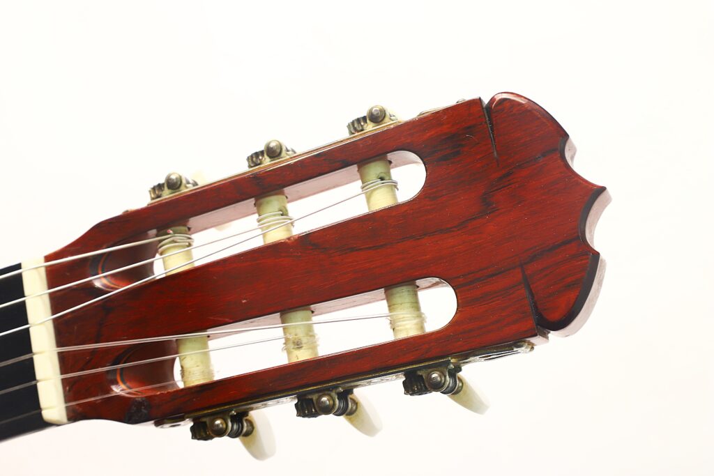 Nahaufnahme des Kopfes einer Jose Ramirez 1a 1977 Klassische Gitarre, die die Stimmwirbel, die Saiten und die dunkle Holzoberfläche vor einem schlichten weißen Hintergrund zeigt. Nahaufnahme des Kopfes einer Jose Ramirez 1a 1977 Klassische Gitarre, die die Stimmwirbel, die Saiten und die dunkle Holzoberfläche vor einem schlichten weißen Hintergrund zeigt.