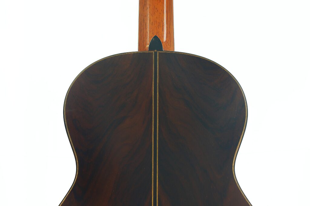 Nahaufnahme der Rückseite einer „Antonius Müller 2004 Doubletop Klassische Gitarre“ mit dunkler Holzmaserung, einem schmalen gelben Mittelstreifen und einem braunen Hals, fotografiert vor weißem Hintergrund. Nahaufnahme der Rückseite einer „Antonius Müller 2004 Doubletop Klassische Gitarre“ mit dunkler Holzmaserung, einem schmalen gelben Mittelstreifen und einem braunen Hals, fotografiert vor weißem Hintergrund.