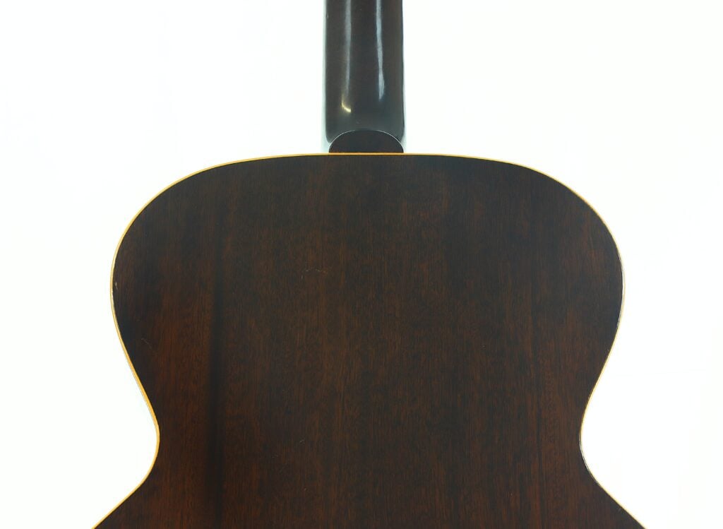 Die Rückseite einer Gibson L-48 Akustikgitarre aus dem Jahr 1948, die ihre dunkle Holzoberfläche und den unteren Teil des Halses vor einem weißen Hintergrund zeigt. Die Rückseite einer Gibson L-48 Akustikgitarre aus dem Jahr 1948, die ihre dunkle Holzoberfläche und den unteren Teil des Halses vor einem weißen Hintergrund zeigt.