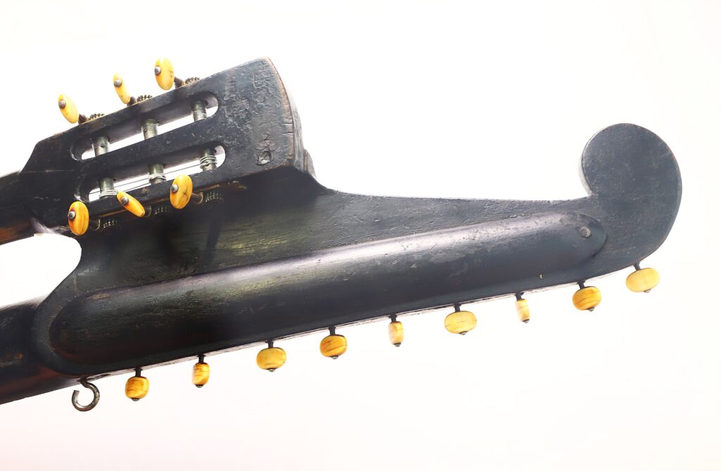 Nahaufnahme des Kopfstücks und des Halses der Kontragitarre „Gustav Keller Stauffer Stil 1900“ aus schwarzem Holz mit gelben Stimmwirbeln und Metall-Stimmmechanik vor weißem Hintergrund. Nahaufnahme des Kopfstücks und des Halses der Kontragitarre „Gustav Keller Stauffer Stil 1900“ aus schwarzem Holz mit gelben Stimmwirbeln und Metall-Stimmmechanik vor weißem Hintergrund.