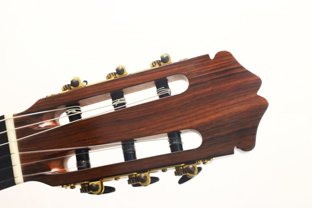 Nahaufnahme des Kopfes einer „Francisco Klassische Gitarre“ von Manuel Adalid Sr. aus dem Jahr 1971, die vor weißem Hintergrund die Holzoberfläche, die Stimmwirbel und die Saiten zeigt. Nahaufnahme des Kopfes einer „Francisco Klassische Gitarre“ von Manuel Adalid Sr. aus dem Jahr 1971, die vor weißem Hintergrund die Holzoberfläche, die Stimmwirbel und die Saiten zeigt.