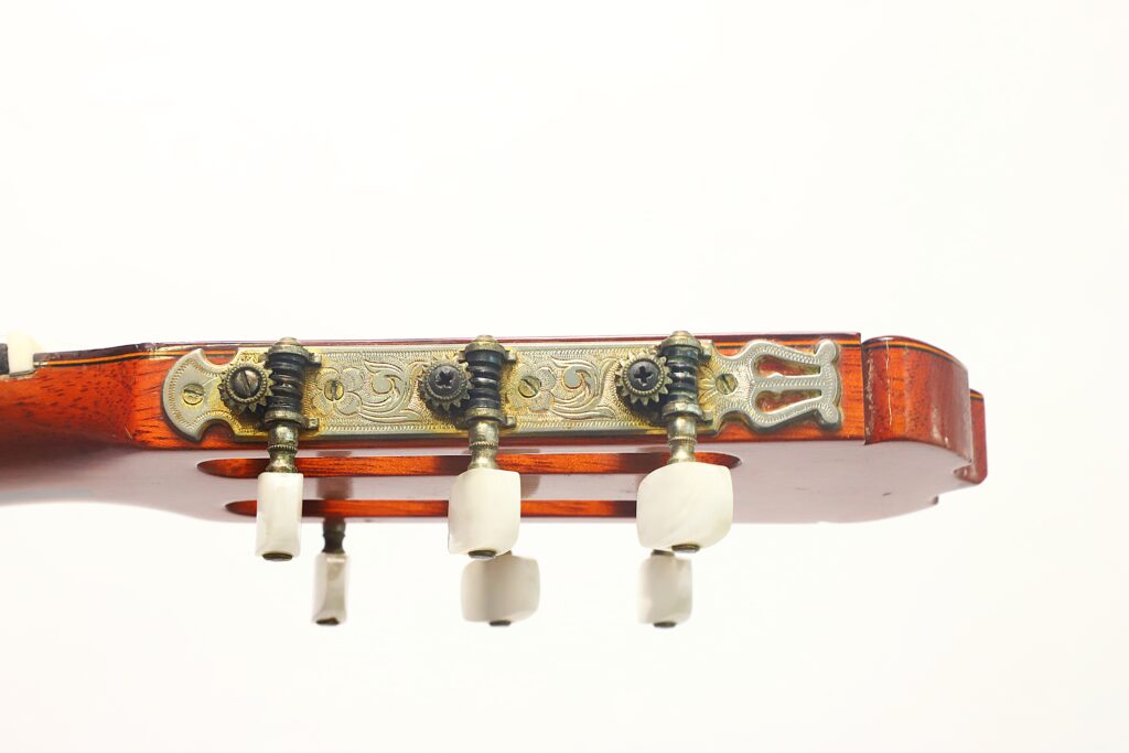 Nahaufnahme der Stimmwirbel und der verzierten Metallplatte am Kopf einer Jose Ramirez 1a 1977 Klassische Gitarre vor weißem Hintergrund. Nahaufnahme der Stimmwirbel und der verzierten Metallplatte am Kopf einer Jose Ramirez 1a 1977 Klassische Gitarre vor weißem Hintergrund.