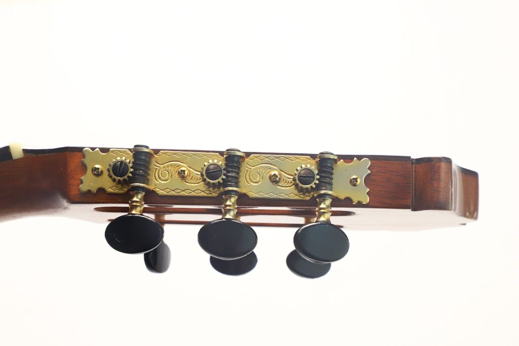Nahaufnahme der Stimmwirbel am Kopf einer „Francisco Klassische Gitarre“ von Manuel Adalid Sr. aus dem Jahr 1971, mit drei schwarzen Stimmwirbeln und goldfarbener Beschlagtechnik vor einem schlichten weißen Hintergrund. Nahaufnahme der Stimmwirbel am Kopf einer „Francisco Klassische Gitarre“ von Manuel Adalid Sr. aus dem Jahr 1971, mit drei schwarzen Stimmwirbeln und goldfarbener Beschlagtechnik vor einem schlichten weißen Hintergrund.