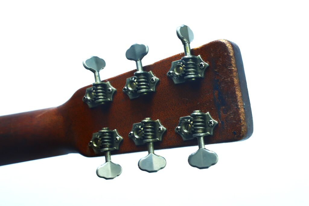 Nahaufnahme der Rückseite des Kopfes einer Martin 000-18 Akustikgitarre aus dem Jahr 1960, auf der sechs Metallstimmwirbel an einem Holzhals zu sehen sind, vor weißem Hintergrund. Nahaufnahme der Rückseite des Kopfes einer Martin 000-18 Akustikgitarre aus dem Jahr 1960, auf der sechs Metallstimmwirbel an einem Holzhals zu sehen sind, vor weißem Hintergrund.