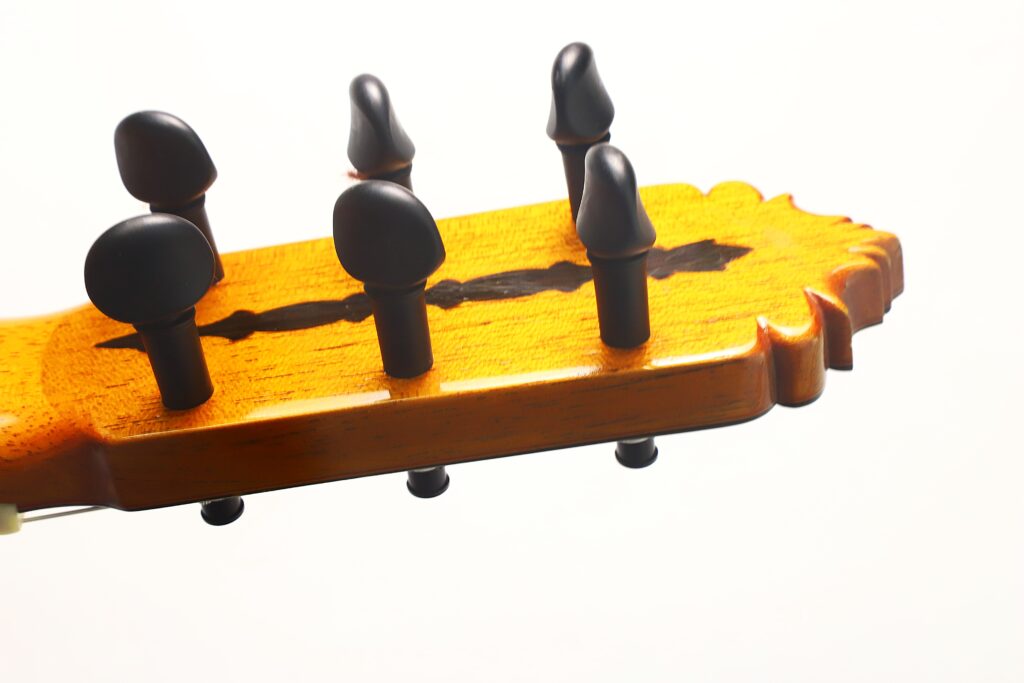 Nahaufnahme des hölzernen Kopfstücks einer Flamenco-Gitarre von Jeronimo Pena aus dem Jahr 1976, auf dem fünf schwarze Stimmwirbel vor weißem Hintergrund zu sehen sind. Nahaufnahme des hölzernen Kopfstücks einer Flamenco-Gitarre von Jeronimo Pena aus dem Jahr 1976, auf dem fünf schwarze Stimmwirbel vor weißem Hintergrund zu sehen sind.
