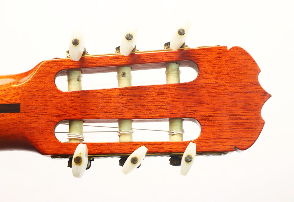 Nahaufnahme des Kopfes einer Jose Ramirez 1a 1977 Klassische Gitarre, die die Stimmwirbel, die weißen Stimmknöpfe und die Nylonsaiten vor weißem Hintergrund zeigt. Nahaufnahme des Kopfes einer Jose Ramirez 1a 1977 Klassische Gitarre, die die Stimmwirbel, die weißen Stimmknöpfe und die Nylonsaiten vor weißem Hintergrund zeigt.