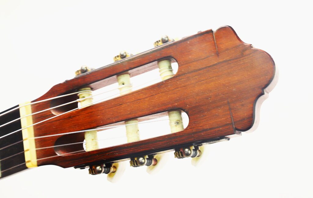 Nahaufnahme des Kopfes einer „Negra Flamenco“-Gitarre von Juan Lopez Aguilarte aus dem Jahr 1984, auf der die Stimmwirbel, die Saiten und die Holzdetails vor weißem Hintergrund zu sehen sind. Nahaufnahme des Kopfes einer „Negra Flamenco“-Gitarre von Juan Lopez Aguilarte aus dem Jahr 1984, auf der die Stimmwirbel, die Saiten und die Holzdetails vor weißem Hintergrund zu sehen sind.