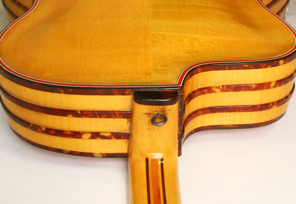 Nahaufnahme der Hals- und Nackenverbindungen von drei übereinander gestapelten Akustikgitarren des Modells „Artur Lang 1950er Jazz-Gitarre“ mit hellen Korpusen und dunkel gestreifter Einfassung, abgebildet vor einem schlichten weißen Hintergrund. Nahaufnahme der Hals- und Nackenverbindungen von drei übereinander gestapelten Akustikgitarren des Modells „Artur Lang 1950er Jazz-Gitarre“ mit hellen Korpusen und dunkel gestreifter Einfassung, abgebildet vor einem schlichten weißen Hintergrund.