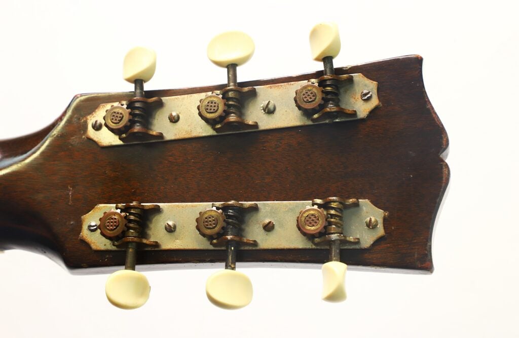 Nahaufnahme der Rückseite des Kopfes einer Gibson L-48 Akustikgitarre aus dem Jahr 1948, die Stimmmechaniken im Vintage-Stil mit cremefarbenen Stimmwirbeln vor weißem Hintergrund zeigt. Nahaufnahme der Rückseite des Kopfes einer Gibson L-48 Akustikgitarre aus dem Jahr 1948, die Stimmmechaniken im Vintage-Stil mit cremefarbenen Stimmwirbeln vor weißem Hintergrund zeigt.