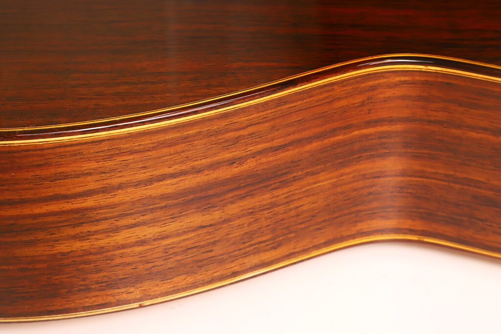 Nahaufnahme der gewölbten Seite einer „Friederich Klassische Gitarre“ von Stefan Nitschke aus dem Jahr 2015, die die glatte, polierte Holzmaserung mit ihren satten Braun- und Goldtönen hervorhebt. Nahaufnahme der gewölbten Seite einer „Friederich Klassische Gitarre“ von Stefan Nitschke aus dem Jahr 2015, die die glatte, polierte Holzmaserung mit ihren satten Braun- und Goldtönen hervorhebt.