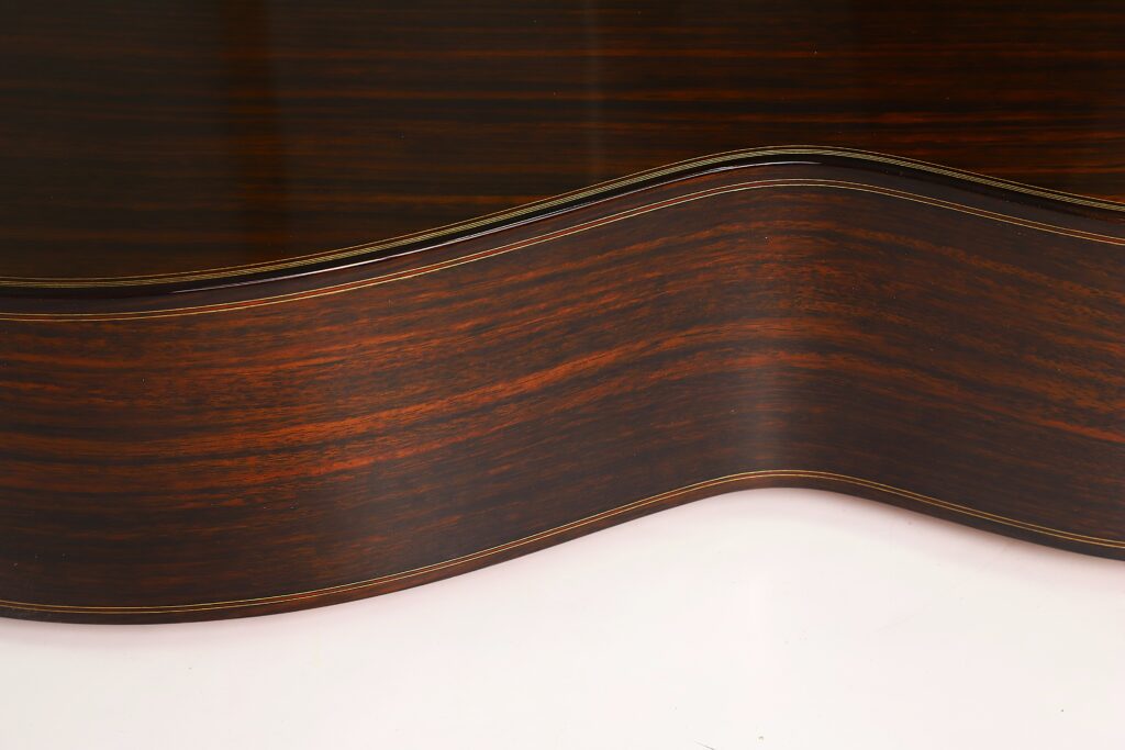 Nahaufnahme der dunklen Holzseite einer „Antonius Müller 2012 Doubletop Klassische Gitarre“, die die satter Holzmaserung und die elegant geschwungene Form vor einem hellen Hintergrund hervorhebt. Nahaufnahme der dunklen Holzseite einer „Antonius Müller 2012 Doubletop Klassische Gitarre“, die die satter Holzmaserung und die elegant geschwungene Form vor einem hellen Hintergrund hervorhebt.