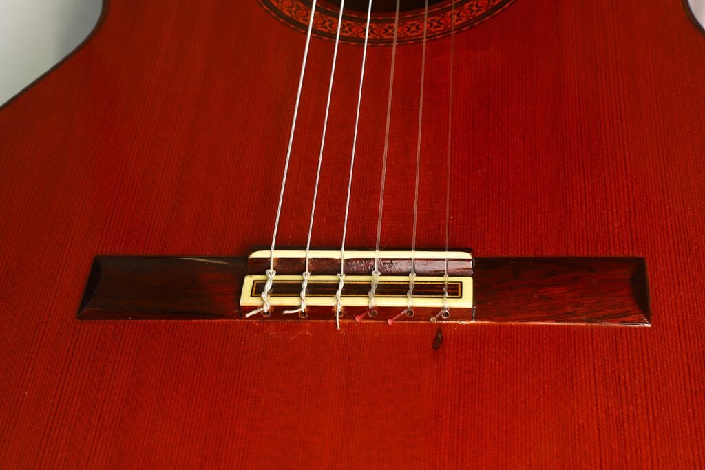 Nahaufnahme der Saiten und des Stegs einer Jose Ramirez 1a 1977 Klassische Gitarre, die die Maserung des Holzes und die feinen Details der Bauweise dieser klassischen Gitarre hervorhebt. Nahaufnahme der Saiten und des Stegs einer Jose Ramirez 1a 1977 Klassische Gitarre, die die Maserung des Holzes und die feinen Details der Bauweise dieser klassischen Gitarre hervorhebt.