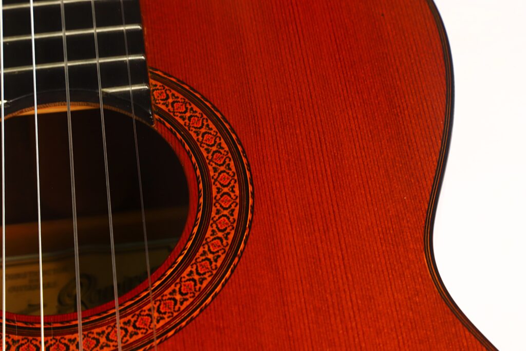 Nahaufnahme des Korpus der Jose Ramirez 1a 1977 Klassische Gitarre, die das Schallloch mit seiner aufwendigen Rosettenverzierung und einen Teil der Saiten auf der linken Seite zeigt und dabei die wunderschöne Holzmaserung sowie die meisterhafte Handwerkskunst hervorhebt. Nahaufnahme des Korpus der Jose Ramirez 1a 1977 Klassische Gitarre, die das Schallloch mit seiner aufwendigen Rosettenverzierung und einen Teil der Saiten auf der linken Seite zeigt und dabei die wunderschöne Holzmaserung sowie die meisterhafte Handwerkskunst hervorhebt.