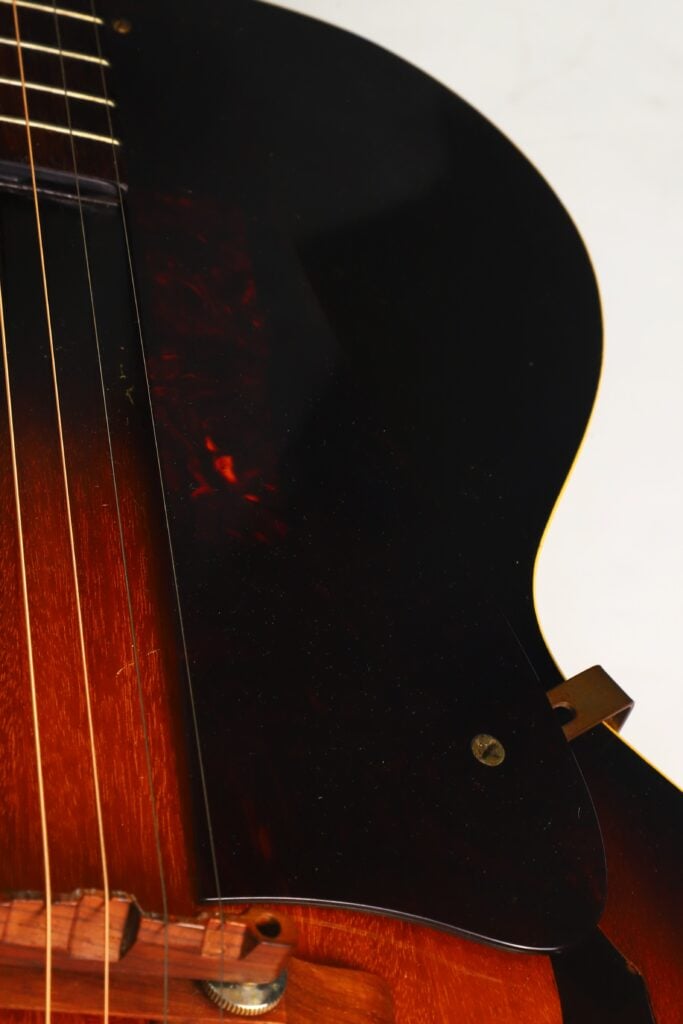 Nahaufnahme des Korpus einer Gibson L-48 Akustikgitarre aus dem Jahr 1948, bei der die Saiten, das dunkle Schlagbrett und ein Teil des Holzstegs hervorgehoben sind, wobei die Oberkante sanft in einen weißen Hintergrund übergeht. Nahaufnahme des Korpus einer Gibson L-48 Akustikgitarre aus dem Jahr 1948, bei der die Saiten, das dunkle Schlagbrett und ein Teil des Holzstegs hervorgehoben sind, wobei die Oberkante sanft in einen weißen Hintergrund übergeht.