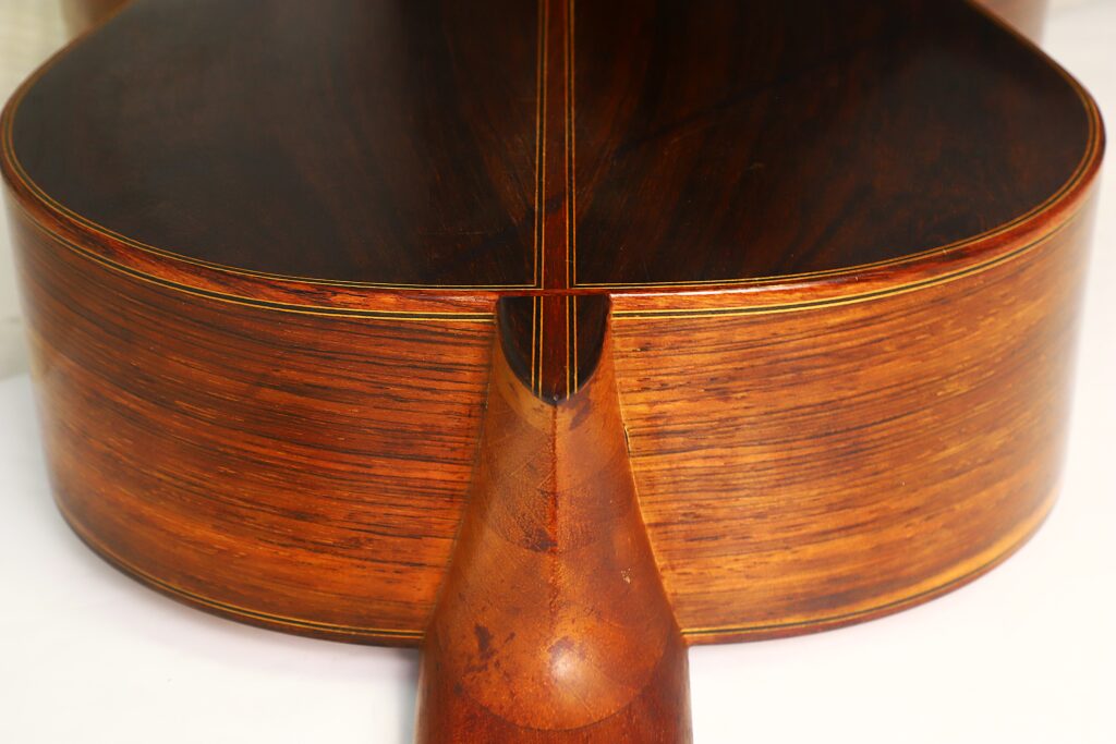 Nahaufnahme des Hals-Korpus-Übergangs einer „Negra Flamenco“-Gitarre von Juan Lopez Aguilarte aus dem Jahr 1984, die vor weißem Hintergrund die satte braune Holzmaserung und die feinen handwerklichen Details hervorhebt. Nahaufnahme des Hals-Korpus-Übergangs einer „Negra Flamenco“-Gitarre von Juan Lopez Aguilarte aus dem Jahr 1984, die vor weißem Hintergrund die satte braune Holzmaserung und die feinen handwerklichen Details hervorhebt.