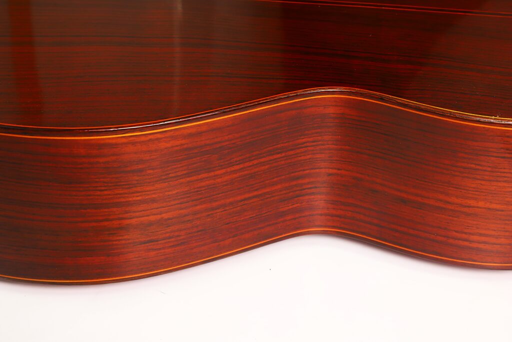 Nahaufnahme der gewölbten Seite einer Jose Ramirez 1a 1977 Klassische Gitarre, die die glatte, polierte Holzmaserung und die satte, rotbraune Farbe vor weißem Hintergrund hervorhebt. Nahaufnahme der gewölbten Seite einer Jose Ramirez 1a 1977 Klassische Gitarre, die die glatte, polierte Holzmaserung und die satte, rotbraune Farbe vor weißem Hintergrund hervorhebt.