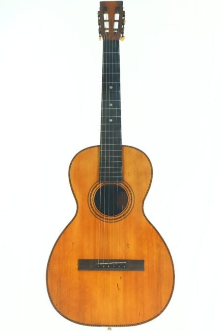 Die Washburn 1900 Parlor Akustik Gitarre verfügt über einen Holzkorpus, ein dunkles Griffbrett und sechs Saiten und wird aufrecht vor einem weißen Hintergrund präsentiert.