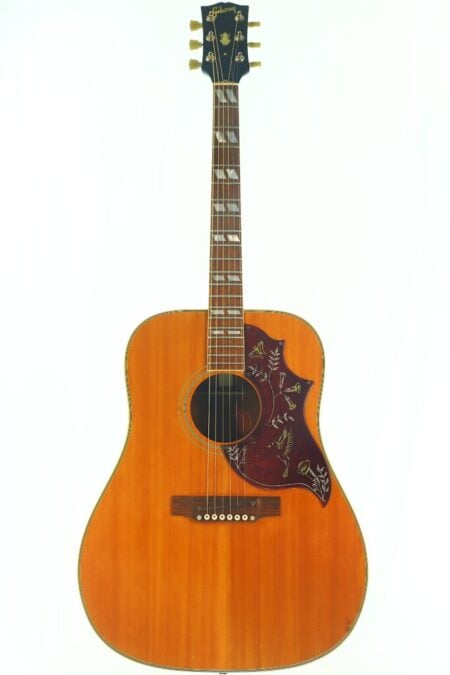 Eine Gibson Hummingbird Akustikgitarre aus dem Jahr 1968 mit naturbelassener Holzoberfläche, einem Pickguard mit Blumenmuster und Perlmutt-Einlagen auf dem Griffbrett.