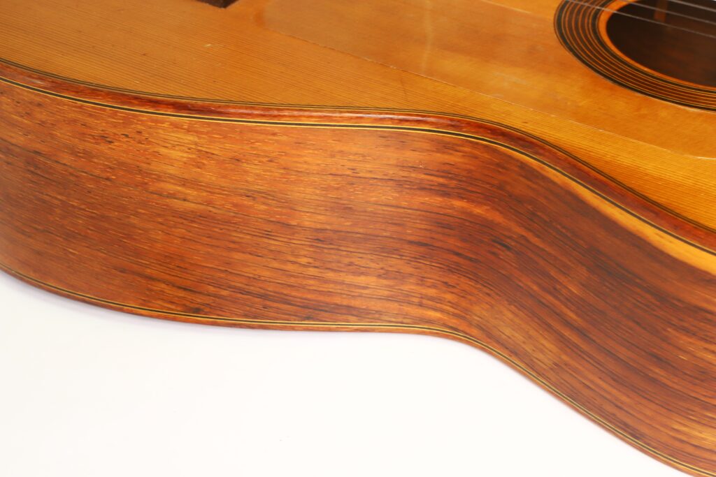 Nahaufnahme der Seite einer „Negra Flamenco“-Gitarre von Juan Lopez Aguilarte aus dem Jahr 1984, die die Holzmaserung und die geschwungene Form des Korpus vor weißem Hintergrund hervorhebt. Nahaufnahme der Seite einer „Negra Flamenco“-Gitarre von Juan Lopez Aguilarte aus dem Jahr 1984, die die Holzmaserung und die geschwungene Form des Korpus vor weißem Hintergrund hervorhebt.