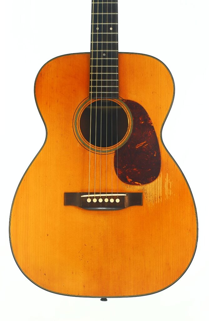Martin 00-18 Akustikgitarre aus dem Jahr 1953 mit naturbelassener Holzoberfläche, dunklem Schlagbrett und sechs Saiten, fotografiert vor weißem Hintergrund. Martin 00-18 Akustikgitarre aus dem Jahr 1953 mit naturbelassener Holzoberfläche, dunklem Schlagbrett und sechs Saiten, fotografiert vor weißem Hintergrund.
