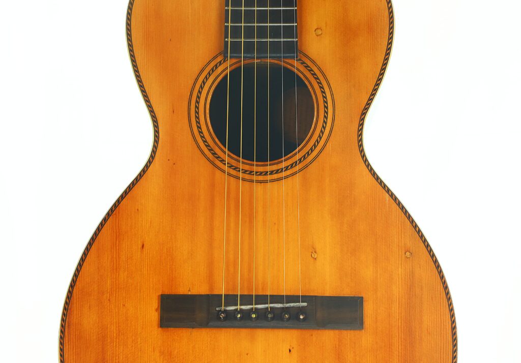 Nahaufnahme des Korpus einer Washburn 1900 Parlor-Akustikgitarre, die die sechs Saiten, das Schallloch mit Zierrand und einen Steg aus Holz vor weißem Hintergrund zeigt. Nahaufnahme des Korpus einer Washburn 1900 Parlor-Akustikgitarre, die die sechs Saiten, das Schallloch mit Zierrand und einen Steg aus Holz vor weißem Hintergrund zeigt.