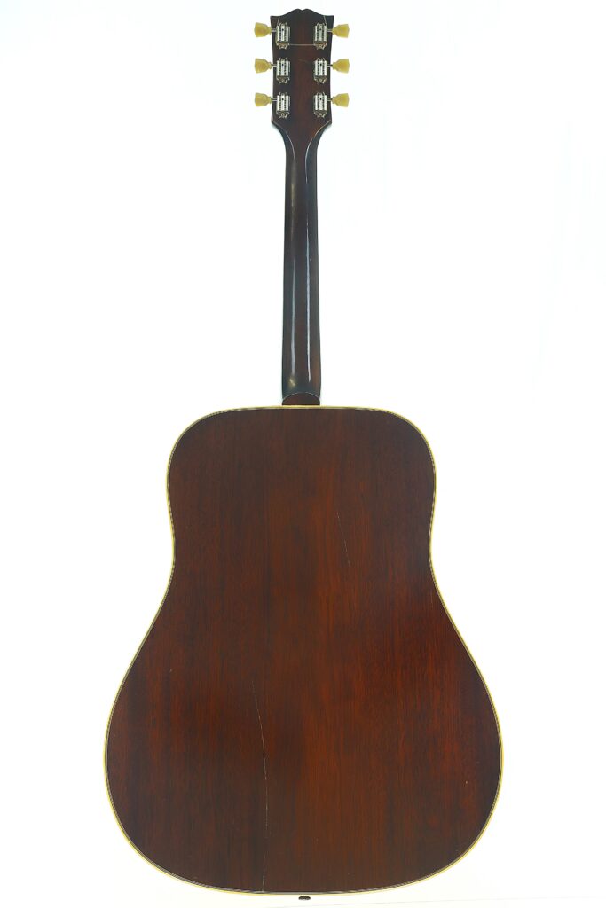 Die Rückansicht der Gibson Hummingbird 1968 Akustikgitarre besticht durch eine dunkle Holzoberfläche, auf der sich Hals, Stimmwirbel und Korpus vor einem weißen Hintergrund abheben. Die Rückansicht der Gibson Hummingbird 1968 Akustikgitarre besticht durch eine dunkle Holzoberfläche, auf der sich Hals, Stimmwirbel und Korpus vor einem weißen Hintergrund abheben.