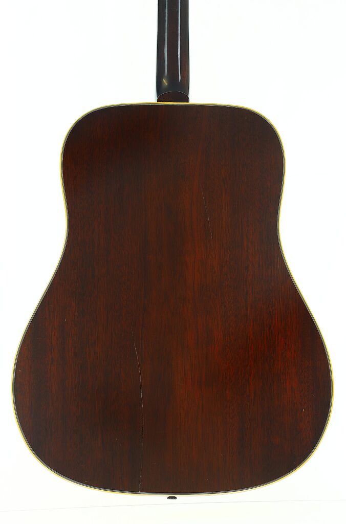 Die Rückansicht der Gibson Hummingbird 1968 Akustikgitarre mit dunkler Holzoberfläche, auf der der Korpus und der untere Teil des Halses vor einem weißen Hintergrund zu sehen sind. Die Rückansicht der Gibson Hummingbird 1968 Akustikgitarre mit dunkler Holzoberfläche, auf der der Korpus und der untere Teil des Halses vor einem weißen Hintergrund zu sehen sind.