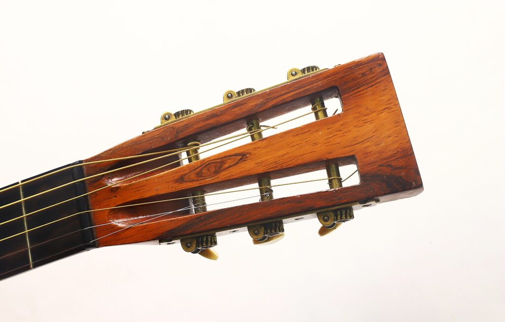Nahaufnahme des Kopfes der Washburn 1900 Parlor Akustikgitarre, die sechs Stimmwirbel und Nylonsaiten zeigt, vor einem schlichten weißen Hintergrund. Nahaufnahme des Kopfes der Washburn 1900 Parlor Akustikgitarre, die sechs Stimmwirbel und Nylonsaiten zeigt, vor einem schlichten weißen Hintergrund.