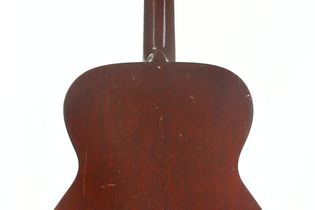 Die Rückseite einer Martin 00-18 Akustikgitarre aus dem Jahr 1953 mit dunkler Holzoberfläche, die einige Kratzer und Gebrauchsspuren aufweist, vor einem schlichten weißen Hintergrund. Die Rückseite einer Martin 00-18 Akustikgitarre aus dem Jahr 1953 mit dunkler Holzoberfläche, die einige Kratzer und Gebrauchsspuren aufweist, vor einem schlichten weißen Hintergrund.