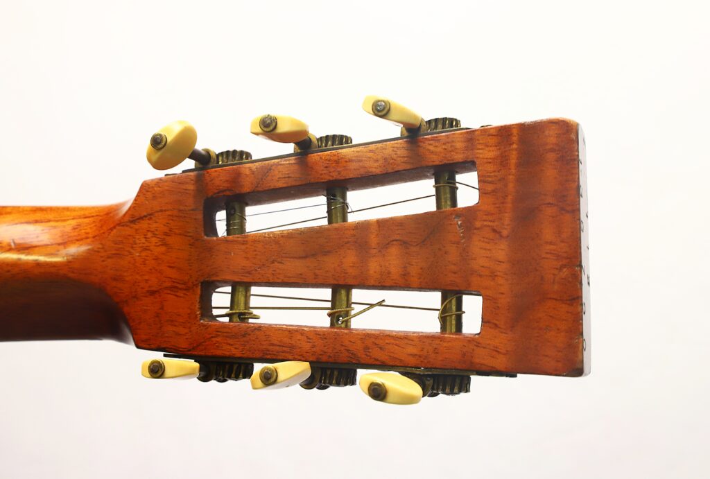 Nahaufnahme des Kopfes der Washburn 1900 Parlor-Akustikgitarre, die vor weißem Hintergrund ihre Holzoberfläche, die offenen Schlitze und die cremefarbenen Stimmwirbel mit Metallzahnrädern zeigt. Nahaufnahme des Kopfes der Washburn 1900 Parlor-Akustikgitarre, die vor weißem Hintergrund ihre Holzoberfläche, die offenen Schlitze und die cremefarbenen Stimmwirbel mit Metallzahnrädern zeigt.