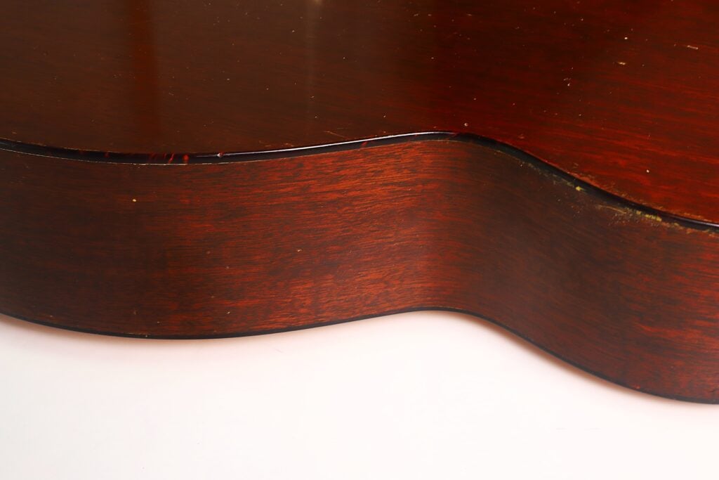 Eine Nahaufnahme der Seite einer Martin 00-18 Akustikgitarre aus dem Jahr 1953 zeigt ihren elegant geschwungenen Korpus, die glatte braune Lackierung und dezente Gebrauchsspuren am Rand – alles vor einem weißen Hintergrund. Eine Nahaufnahme der Seite einer Martin 00-18 Akustikgitarre aus dem Jahr 1953 zeigt ihren elegant geschwungenen Korpus, die glatte braune Lackierung und dezente Gebrauchsspuren am Rand – alles vor einem weißen Hintergrund.