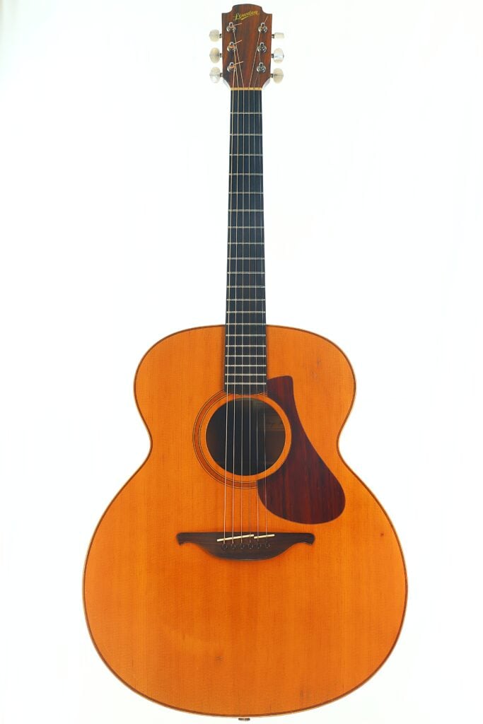 Eine Lowden G-7 Akustikgitarre aus den 1980er Jahren mit naturbelassener Holzoberfläche, schwarzem Griffbrett, sechs Saiten und einem dunkelbraunen Schlagbrett, fotografiert vor einem schlichten weißen Hintergrund. Eine Lowden G-7 Akustikgitarre aus den 1980er Jahren mit naturbelassener Holzoberfläche, schwarzem Griffbrett, sechs Saiten und einem dunkelbraunen Schlagbrett, fotografiert vor einem schlichten weißen Hintergrund.
