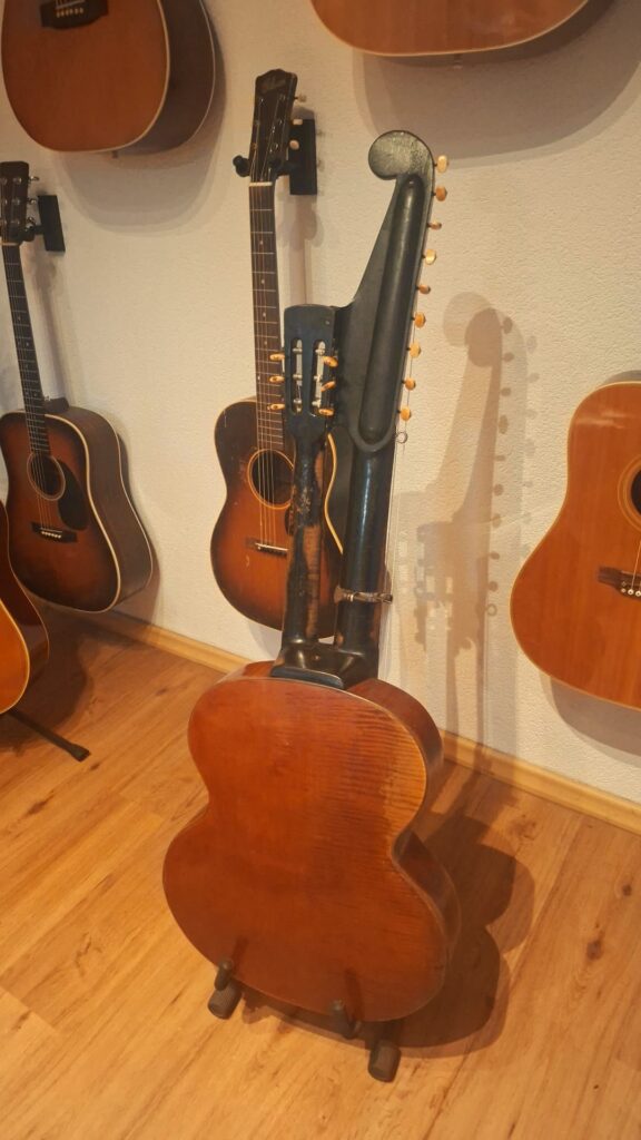 Die „Gustav Keller Stauffer Stil 1900 Kontragitarre“, eine einzigartige Harfengitarre mit mehreren Hälsen und Saiten, steht zusammen mit anderen traditionellen Akustikgitarren auf einem Holzboden vor einer weißen Wand. Die „Gustav Keller Stauffer Stil 1900 Kontragitarre“, eine einzigartige Harfengitarre mit mehreren Hälsen und Saiten, steht zusammen mit anderen traditionellen Akustikgitarren auf einem Holzboden vor einer weißen Wand.
