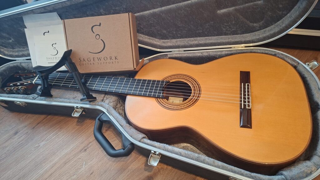Eine Friederich-Klassikgitarre von Stefan Nitschke aus dem Jahr 2015 ruht in einem grau gefütterten Hartschalenkoffer, daneben liegen auf einem Holzboden ein Sagework-Gitarrenständer, eine Gebrauchsanweisung und eine Schachtel. Eine Friederich-Klassikgitarre von Stefan Nitschke aus dem Jahr 2015 ruht in einem grau gefütterten Hartschalenkoffer, daneben liegen auf einem Holzboden ein Sagework-Gitarrenständer, eine Gebrauchsanweisung und eine Schachtel.