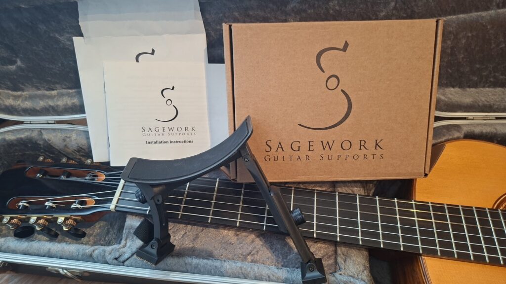 Eine Sagework-Gitarrenstütze ruht auf einer „Friederich Klassische Gitarre“ von Stefan Nitschke aus dem Jahr 2015 in einem offenen Koffer, hinter der eine Sagework-Box und Bedienungsanleitungen zu sehen sind. Eine Sagework-Gitarrenstütze ruht auf einer „Friederich Klassische Gitarre“ von Stefan Nitschke aus dem Jahr 2015 in einem offenen Koffer, hinter der eine Sagework-Box und Bedienungsanleitungen zu sehen sind.