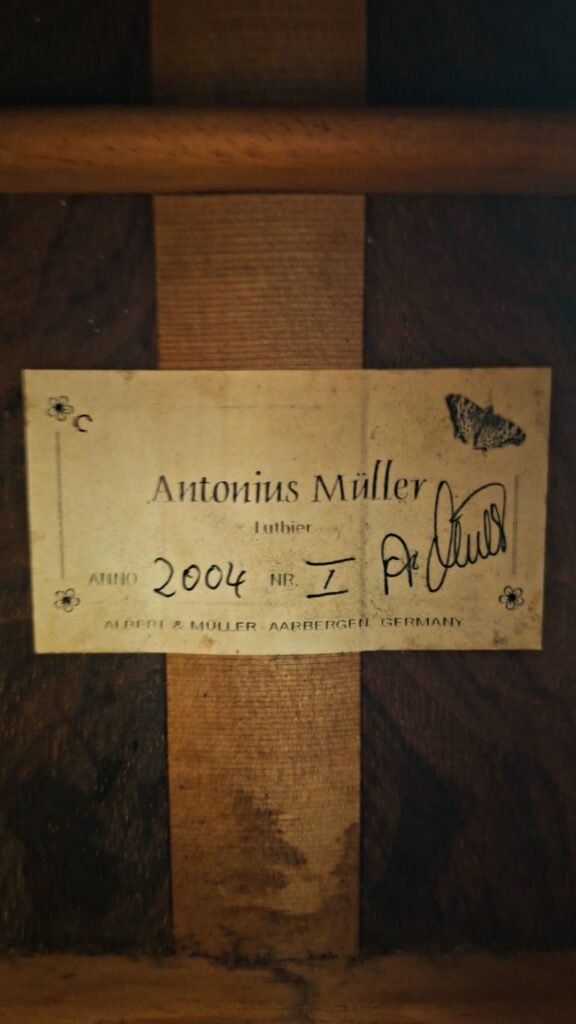 Auf einem Etikett im Inneren eines Holzinstruments steht: Antonius Müller 2004 Doubletop Klassische Gitarre, Gitarrenbauer, Nr. 1, ALBERT & MÜLLER AARBURG-GERMANY; eine Unterschrift und eine eingerissene Ecke sind zu sehen. Auf einem Etikett im Inneren eines Holzinstruments steht: Antonius Müller 2004 Doubletop Klassische Gitarre, Gitarrenbauer, Nr. 1, ALBERT & MÜLLER AARBURG-GERMANY; eine Unterschrift und eine eingerissene Ecke sind zu sehen.