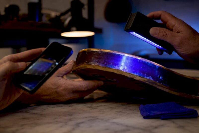 Hands checking guitar finish under blacklight